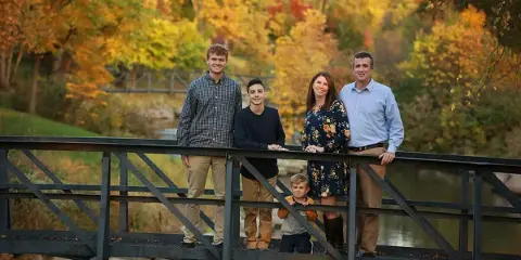 A family of five posing on a metal bridge in a park with autumn foliage.