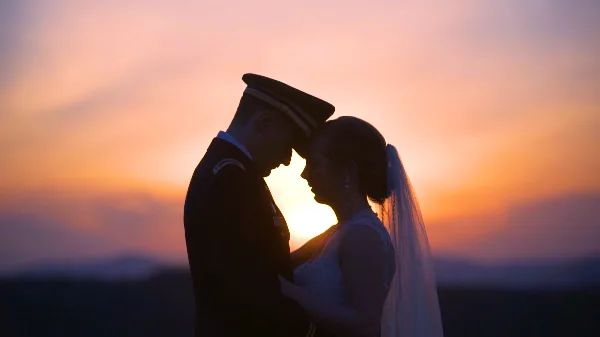 A silhouette of a bride and groom in a military uniform touching foreheads against a vibrant sunset sky.