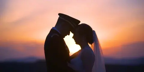 A silhouette of a bride and groom in a military uniform touching foreheads against a vibrant sunset sky.