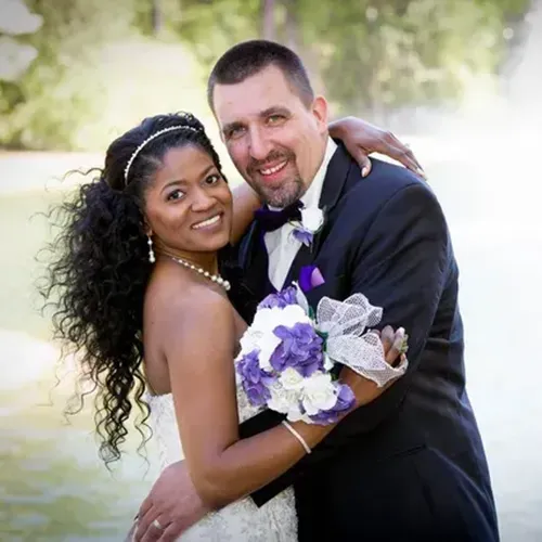 A bride and groom posing for a portrait outdoors near a lake.