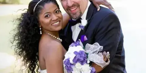 A bride and groom posing for a portrait outdoors near a lake.