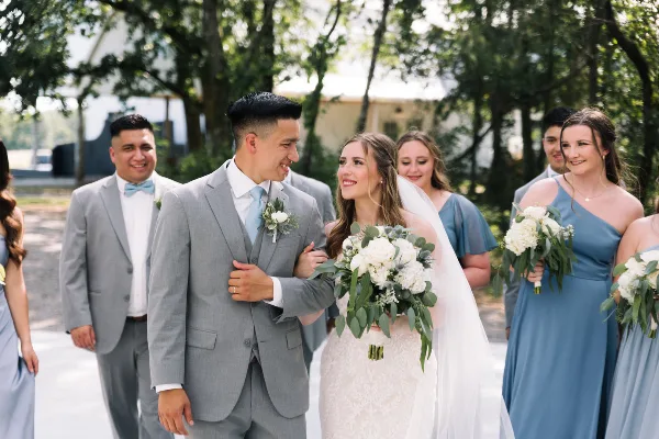 A bride and groom smiling together with their wedding party outdoors.