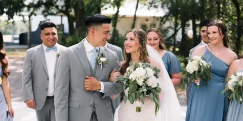 A bride and groom smiling together with their wedding party outdoors.