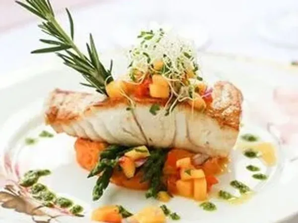 A plated gourmet fish dish with asparagus, diced vegetables, and a rosemary sprig garnish.