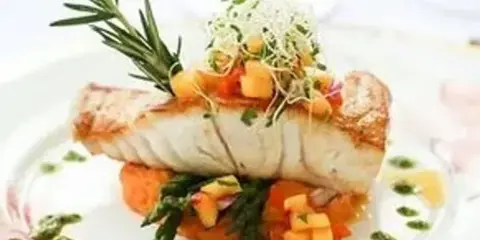 A plated gourmet fish dish with asparagus, diced vegetables, and a rosemary sprig garnish.