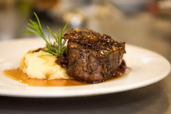 A plated main course featuring a seared meat medallion with mashed potatoes, gravy, and a rosemary garnish.