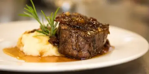 A plated main course featuring a seared meat medallion with mashed potatoes, gravy, and a rosemary garnish.