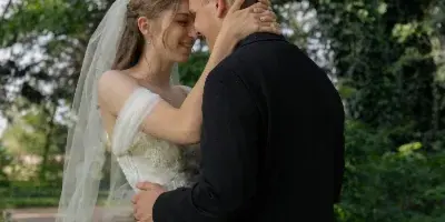 A bride in a white gown and veil and a groom in a black suit embracing and smiling in a garden setting.