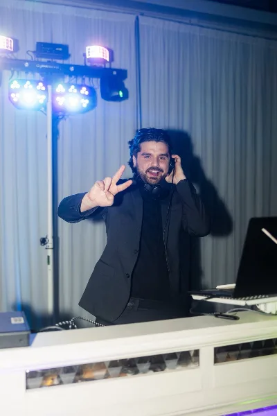 A DJ in a black suit performing at an event with stage lighting and audio equipment.