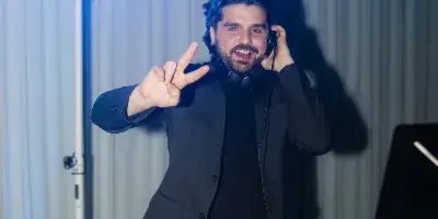 A DJ in a black suit performing at an event with stage lighting and audio equipment.