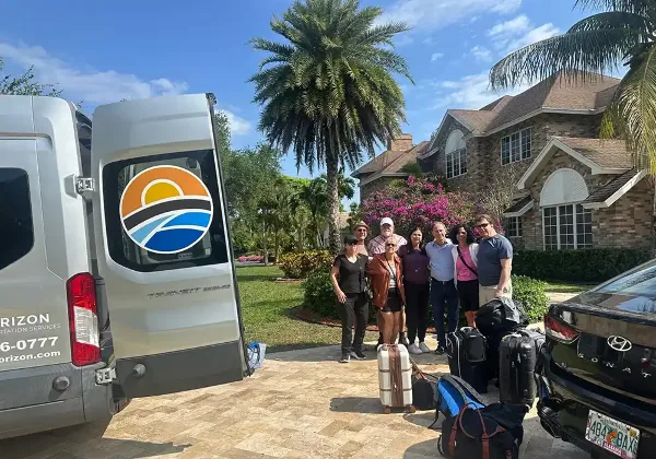 A group of people with luggage standing next to a white Horizon Transportation Services van parked in a driveway.