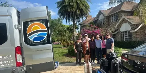 A group of people with luggage standing next to a white Horizon Transportation Services van parked in a driveway.