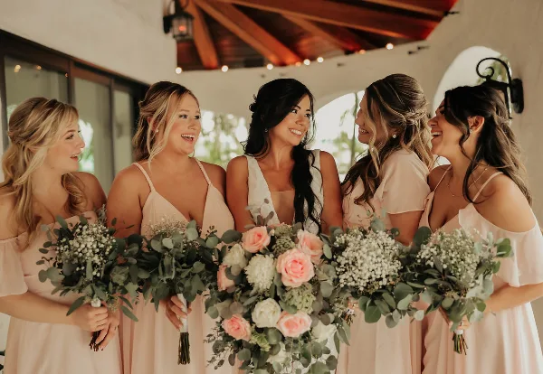A bride and four bridesmaids with styled hair and makeup holding bouquets.