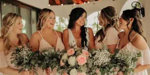 A bride and four bridesmaids with styled hair and makeup holding bouquets.
