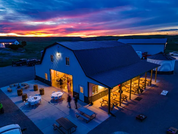 Aerial view of a white barn event center with a covered patio and picnic tables at sunset.