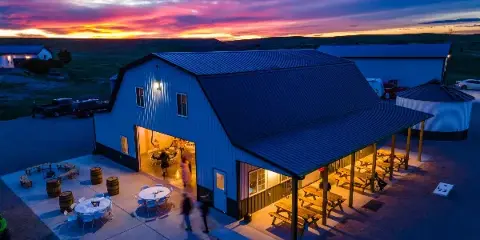 Aerial view of a white barn event center with a covered patio and picnic tables at sunset.