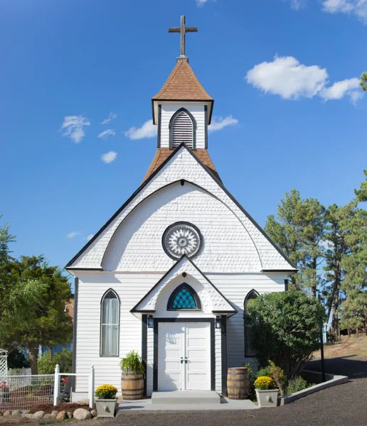 Exterior view of a white historic chapel with a steeple and cross under a blue sky.