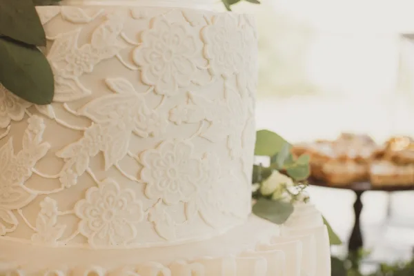 Close-up of a white wedding cake with detailed floral sugar decorations and greenery accents.