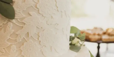 Close-up of a white wedding cake with detailed floral sugar decorations and greenery accents.