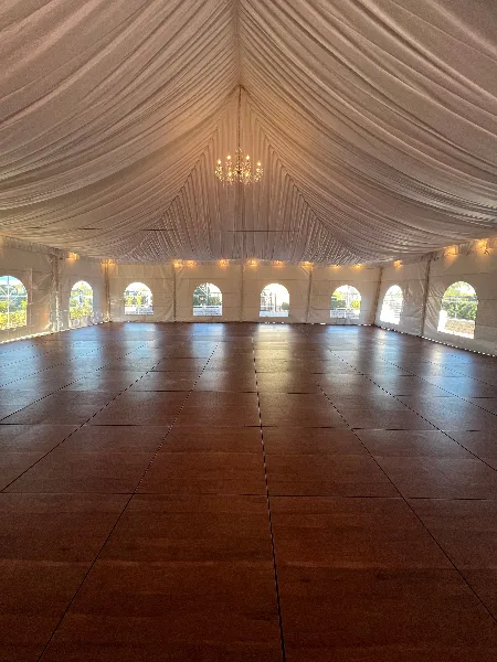 Interior of a large white event tent featuring a wooden dance floor and a hanging chandelier.
