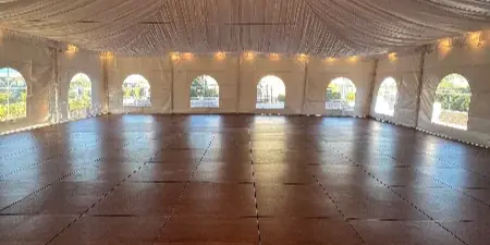 Interior of a large white event tent featuring a wooden dance floor and a hanging chandelier.
