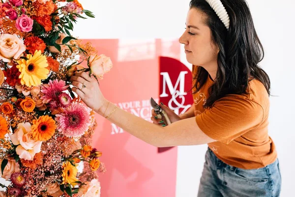 A floral designer arranging a colorful bouquet of roses and gerbera daisies in a studio setting.