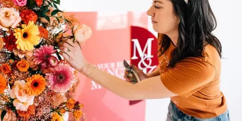 A floral designer arranging a colorful bouquet of roses and gerbera daisies in a studio setting.