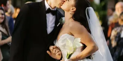 A bride and groom share a kiss during their wedding ceremony, with the bride holding a bouquet of white calla lilies.