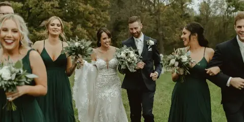 A bride and groom walking with their wedding party in an outdoor setting.