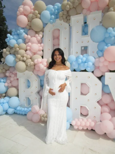 A woman in a white dress standing in front of a large balloon arch and illuminated marquee letters.