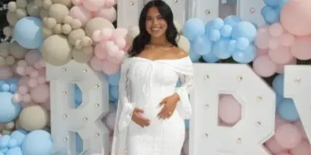 A woman in a white dress standing in front of a large balloon arch and illuminated marquee letters.