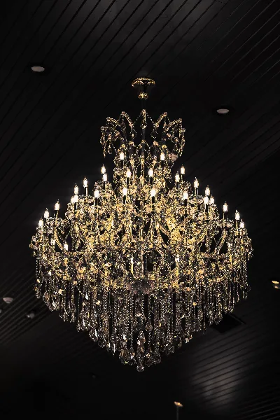 A large, ornate crystal chandelier with lit bulbs hanging from a dark, slatted ceiling.