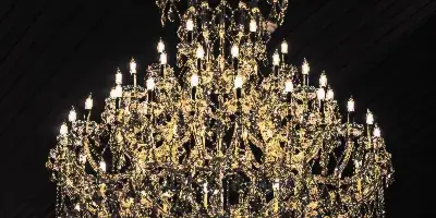 A large, ornate crystal chandelier with lit bulbs hanging from a dark, slatted ceiling.