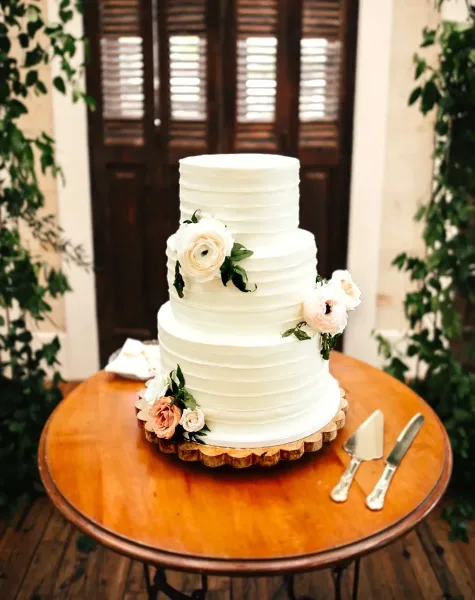 A three-tiered white wedding cake with horizontal ridges and floral decorations on a wooden table.