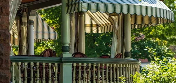 Outdoor dining porch with green and white striped awnings and wicker chairs at a restaurant.