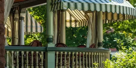 Outdoor dining porch with green and white striped awnings and wicker chairs at a restaurant.