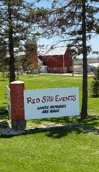 A white sign reading 'Red Silo Events' stands on a grassy lawn in front of a red barn and silo.