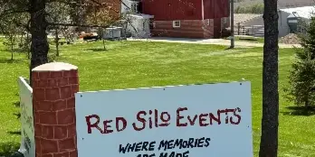 A white sign reading 'Red Silo Events' stands on a grassy lawn in front of a red barn and silo.