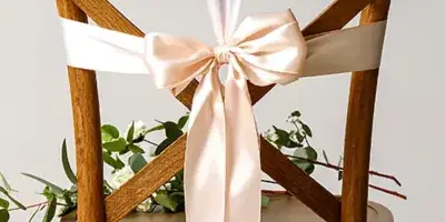 A wooden cross-back chair decorated with a white and pink sash and greenery.
