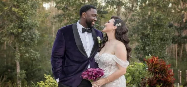 Bride with styled wavy hair and hair accessory standing with groom outdoors holding a bouquet