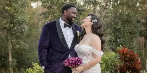 Bride with styled wavy hair and hair accessory standing with groom outdoors holding a bouquet