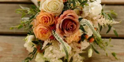 A wedding bouquet with peach and white roses, greenery, and filler flowers resting on a wooden surface.