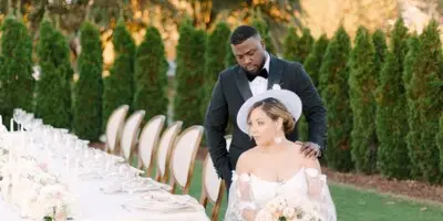 A bride and groom posing together at an outdoor wedding reception with a long floral table setting.