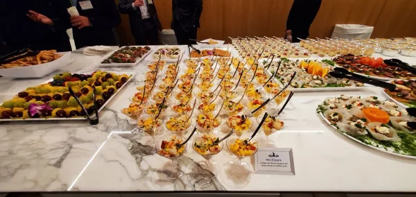 A wide shot of a catering table filled with various appetizers, fruit platters, and individual servings in martini glasses.