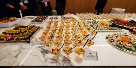 A wide shot of a catering table filled with various appetizers, fruit platters, and individual servings in martini glasses.