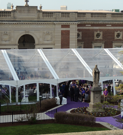A large clear event tent set up for a wedding reception with a purple carpet aisle and guests inside.