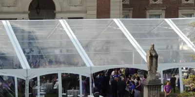 A large clear event tent set up for a wedding reception with a purple carpet aisle and guests inside.