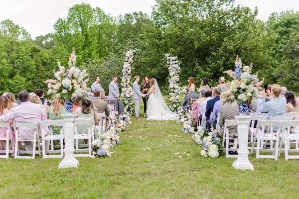 Outdoor wedding ceremony with bride and groom at a floral altar and seated guests.