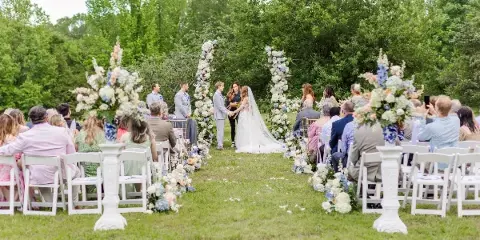 Outdoor wedding ceremony with bride and groom at a floral altar and seated guests.