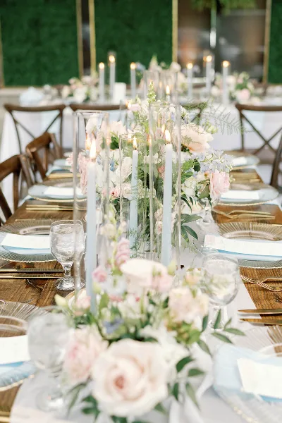 Elegant wedding table setting featuring tall glass candle holders, floral arrangements, and gold-rimmed plates.